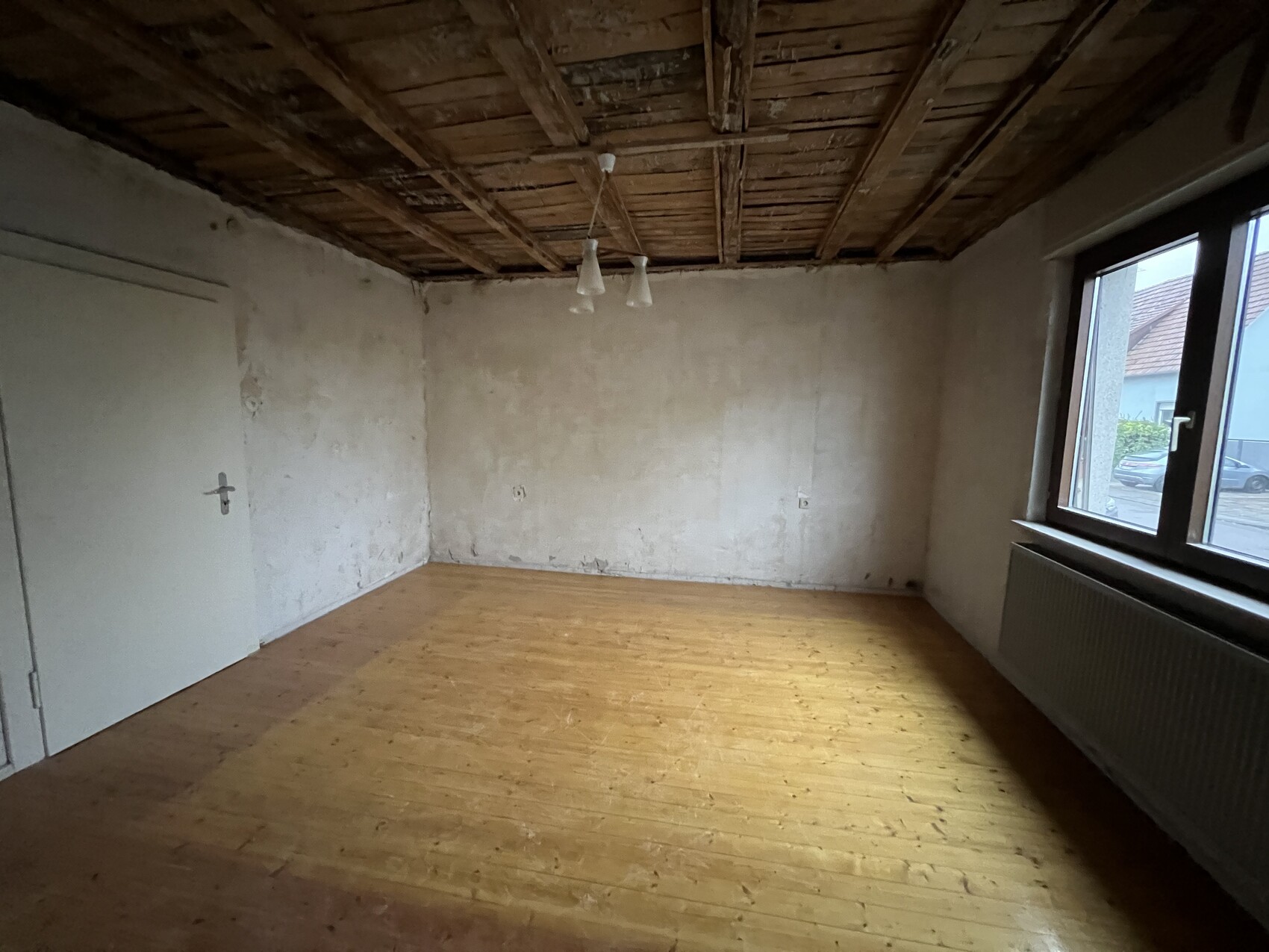 Leerraum mit Holzfußboden, rohen Wänden, sichtbaren Deckenbalken und Fenster rechts