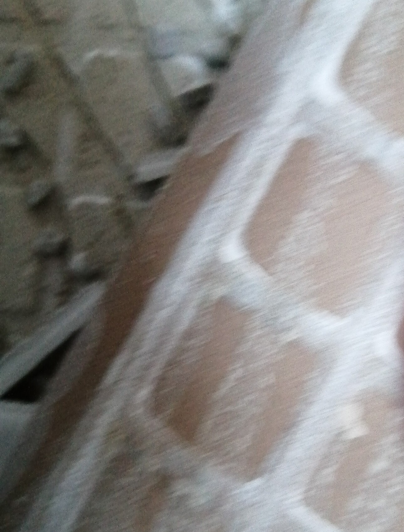 Nahaufnahme eines braun-weißen Stoffes mit Muster, unscharf, Steinwand im Hintergrund
