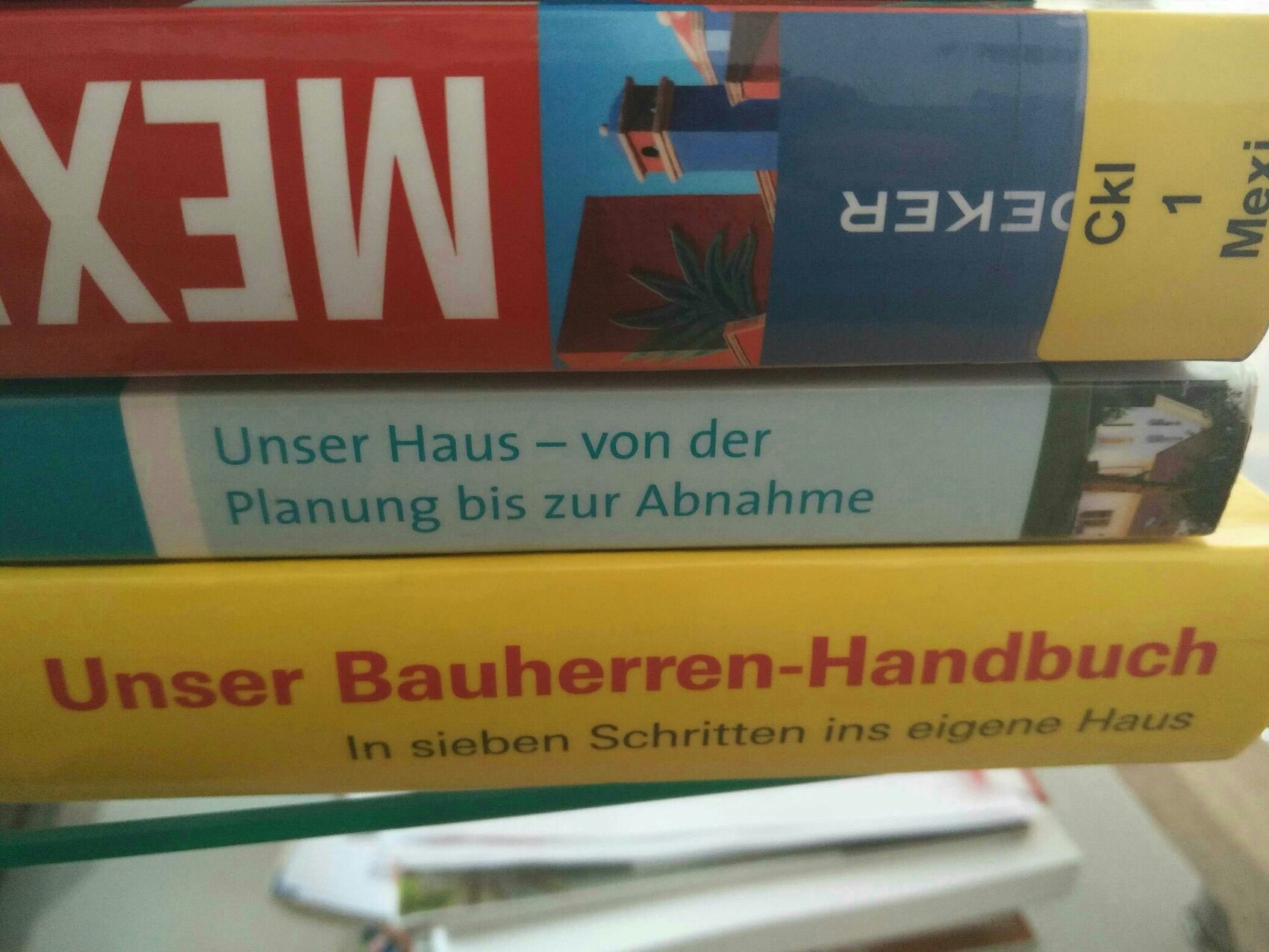 Bücherstapel mit Titeln zu Hausplanung und Bauhandbuch in bunten Buchrücken