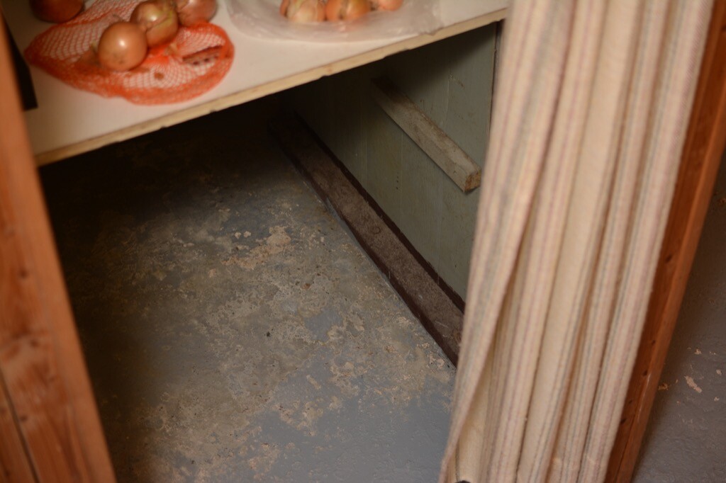 Kellerabstellraum mit Zwiebeln auf Regal und schmutzigem Boden hinter Vorhang