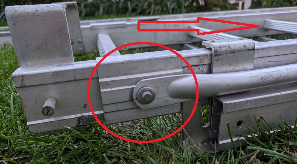 Metallrahmen aus Aluminium mit Gelenkbolzen am Schwenkarm, auf Gras liegend.
