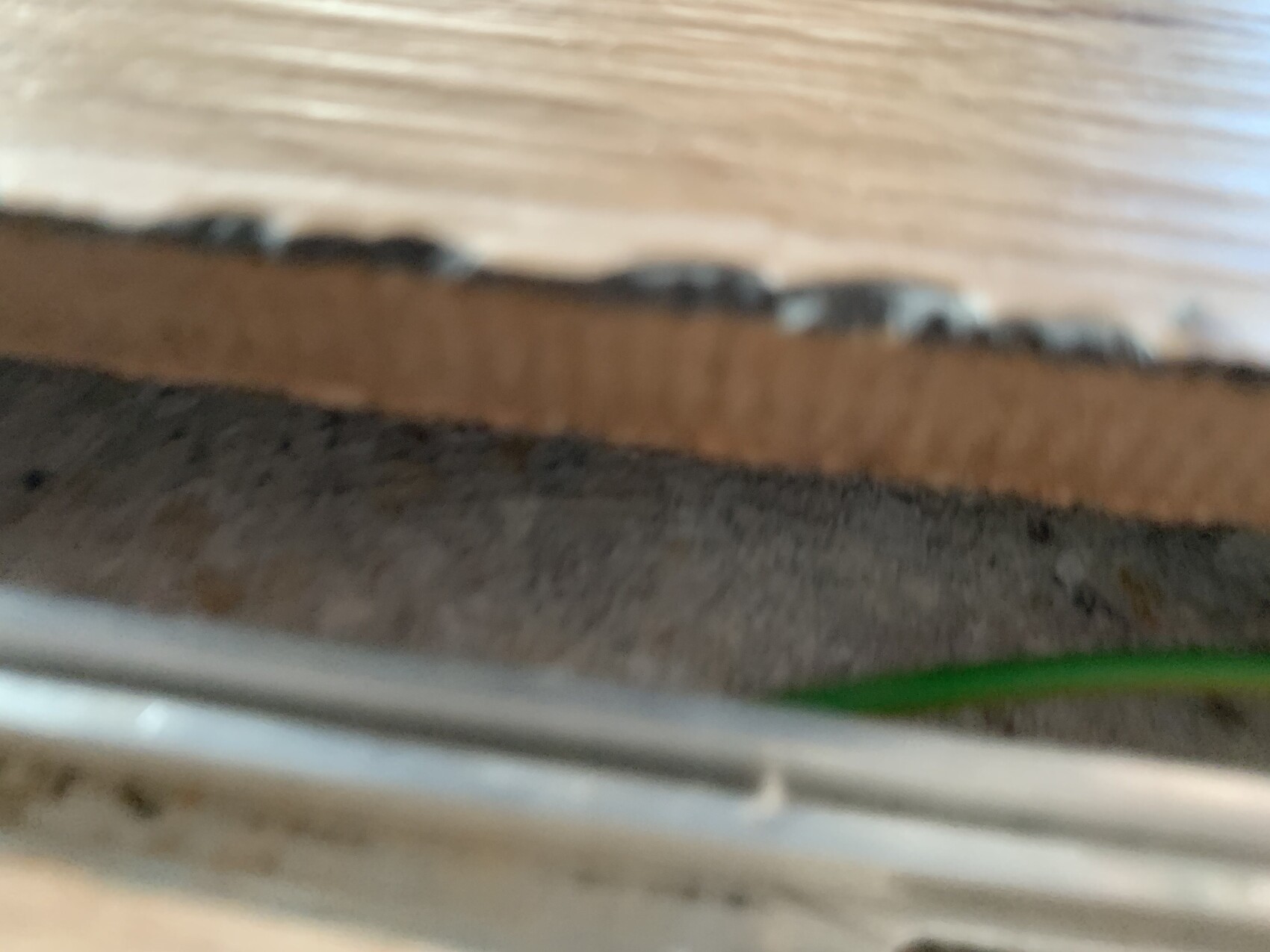 Sehr unscharfes Foto von Holzdiele, brauner Kante, grauer Unterlage und grünem Kabel.