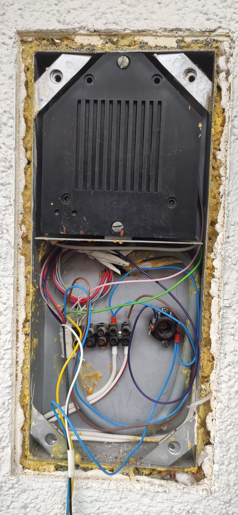 Offener Wandkasten mit vielen bunten Kabeln und einem schwarzen Elektronikmodul.