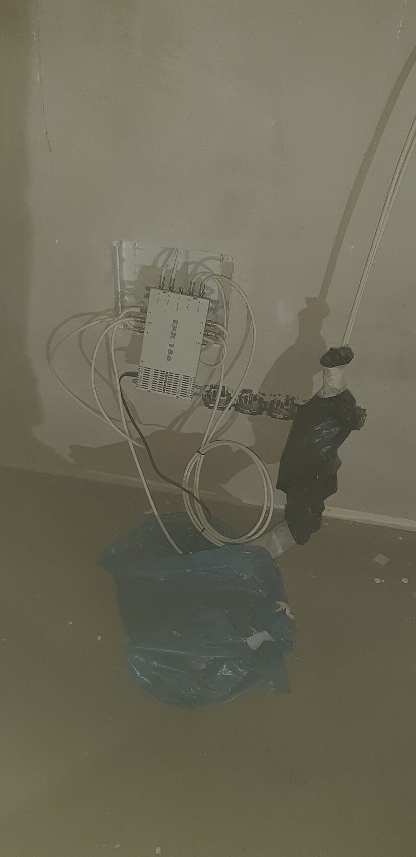 Elektrischer Verteilkasten mit Kabeln (EXR 156) an der Wand; blauer Müllsack am Boden.