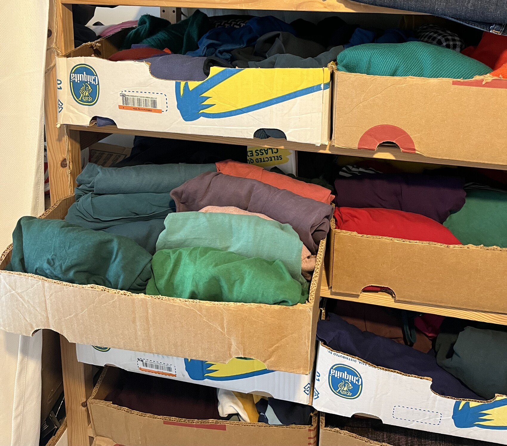 Offene Kartonboxen mit bunt gefalteter Kleidung in einem Kleiderschrank
