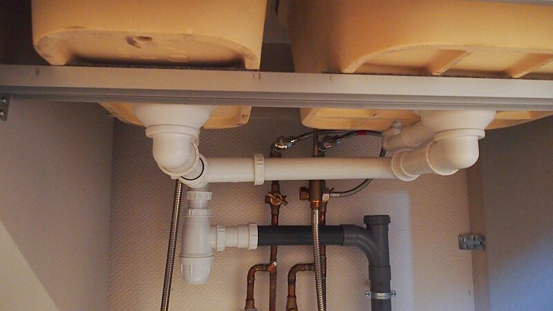 Unter dem Spülbecken sichtbare Abfluss- und Versorgungsrohre aus PVC und Kupfer.