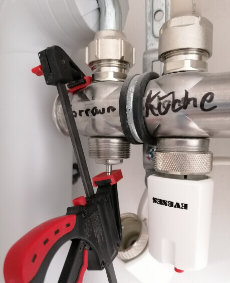Unter dem Spülbecken: Rohrleitungen, zwei Absperrventile und ein Messgerät.