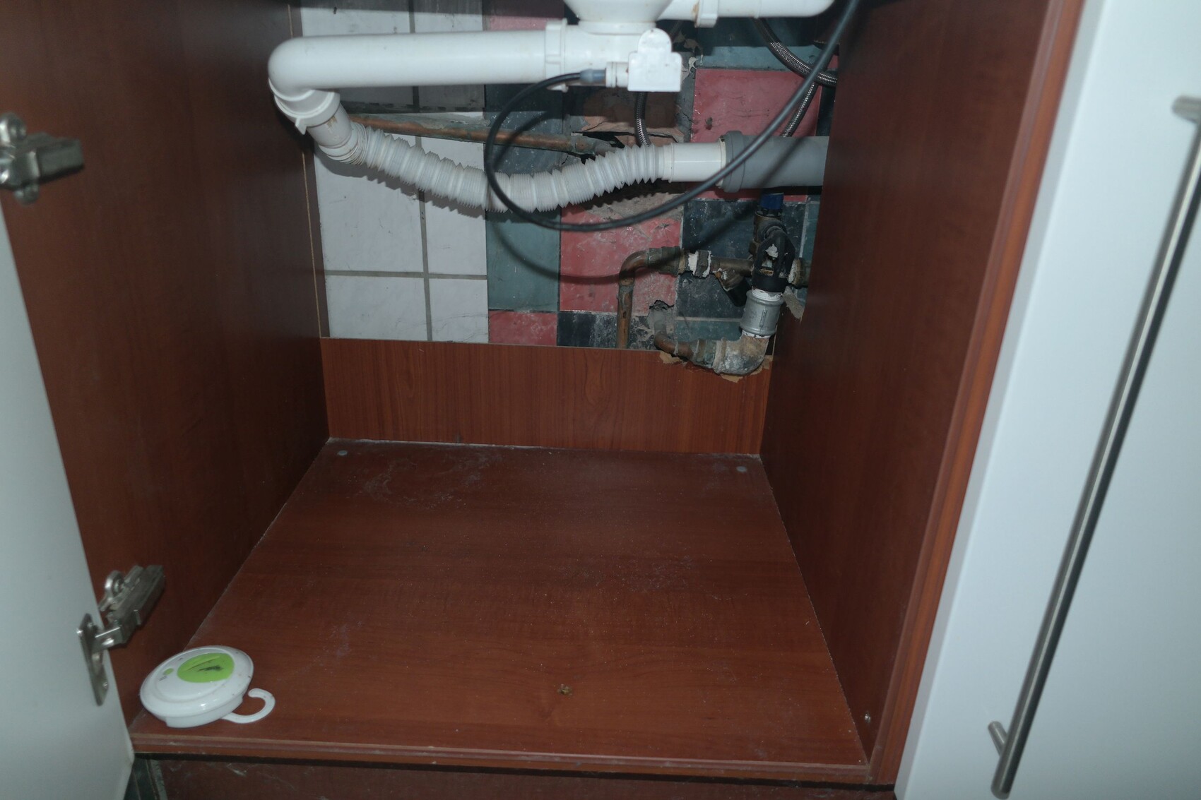 Unter dem Spülbecken: sichtbare Leitungen, Abflussrohr und bunte Fliesen im Schrank.