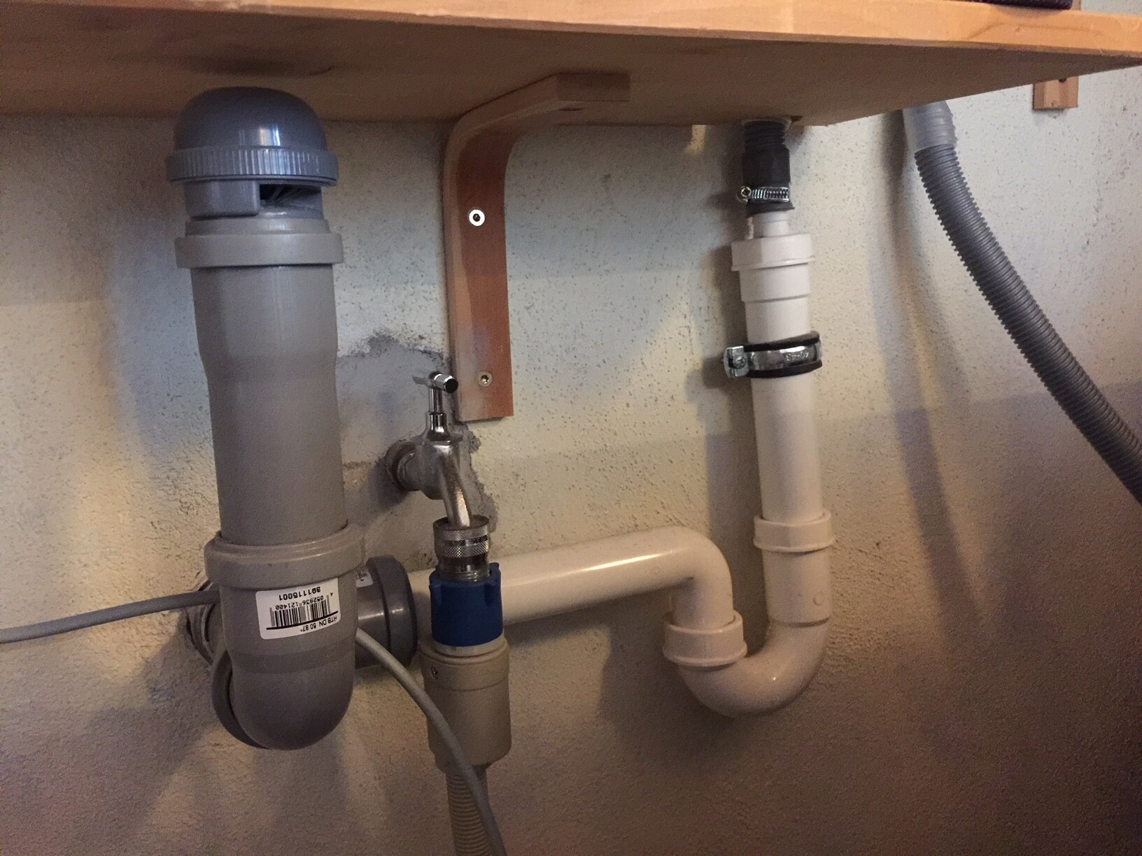 Unter dem Spülbecken sichtbare PVC-Abflussrohre, Siphon, blaues Absperrventil, Klemmen.