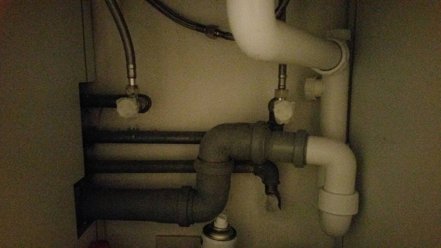 Unter dem Spülbecken sichtbare Rohrleitungen und Sanitärverbindungen.