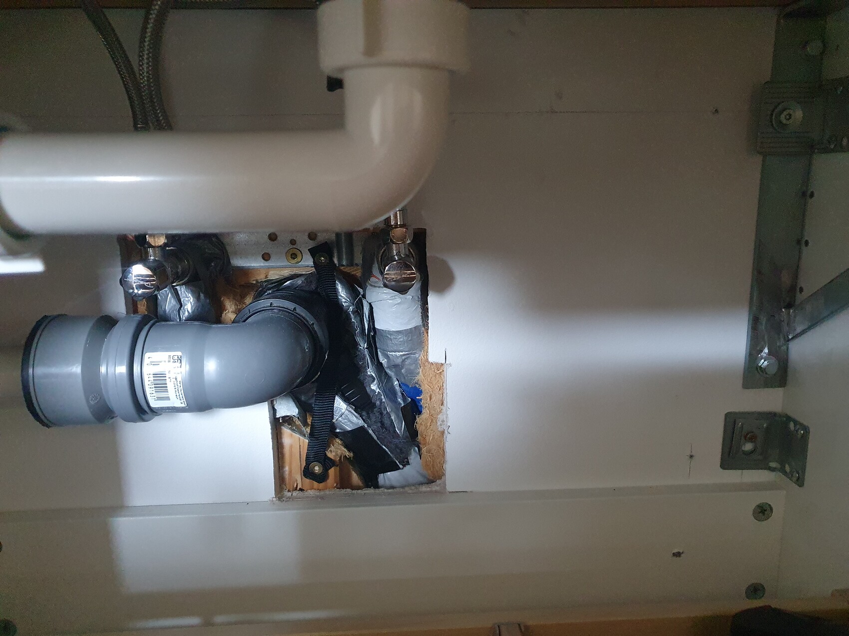 Unter dem Spülbecken sichtbare PVC-Abflussrohre mit S-förmiger Verbindung und Loch in der Wand.