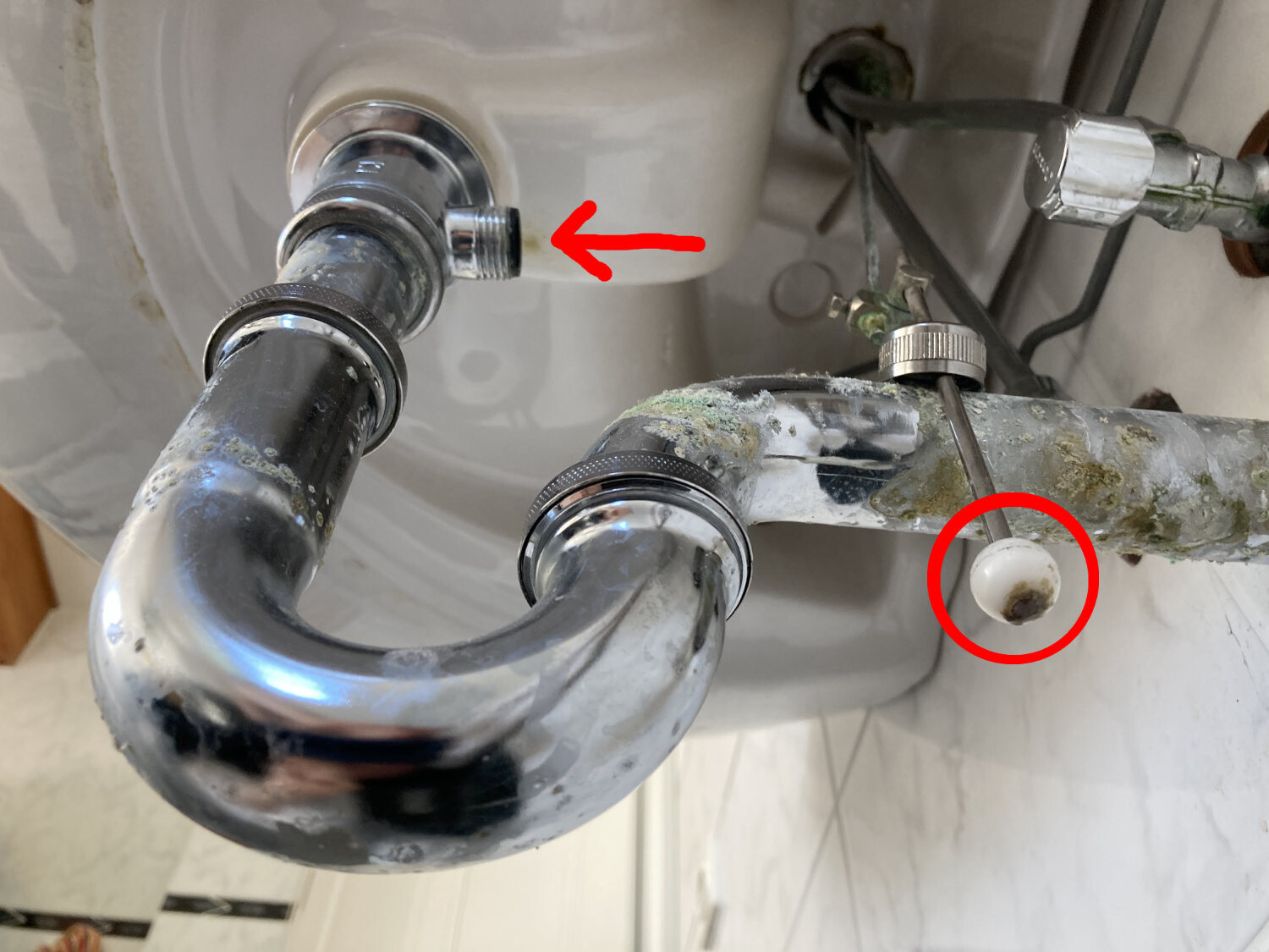 Unter der Spüle: verchromter Siphon, rostanfällige Rohre; weiße Kugel mit Fleck am Rohr.