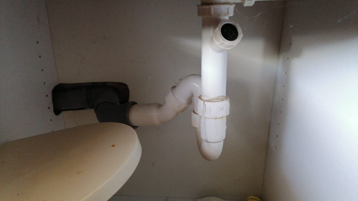 Unter dem Waschbecken sichtbarer weißer PVC-Siphon mit P-Trap und Abflussverbindung.
