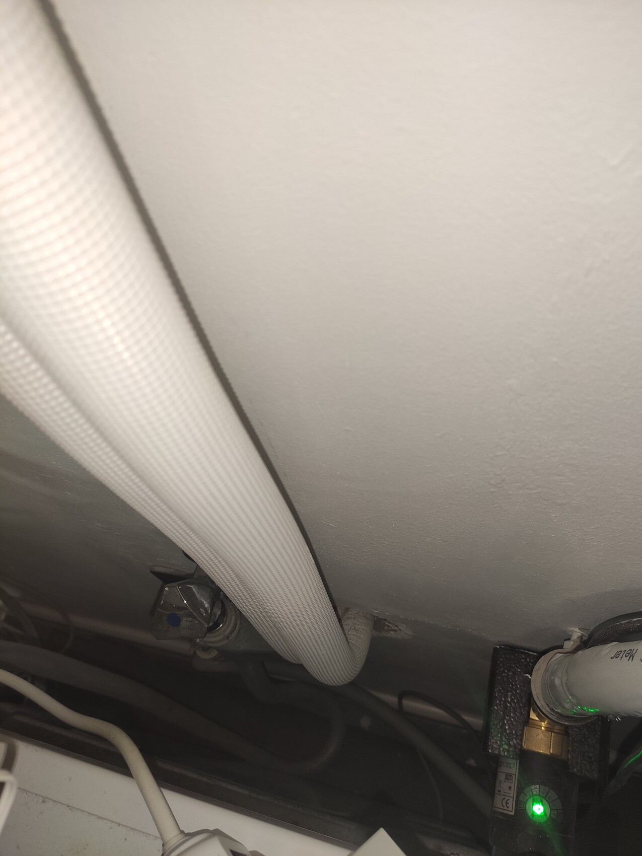 Weiße flexible Leitung verläuft entlang einer Metalloberfläche; rechts Ventil mit grünem Licht.