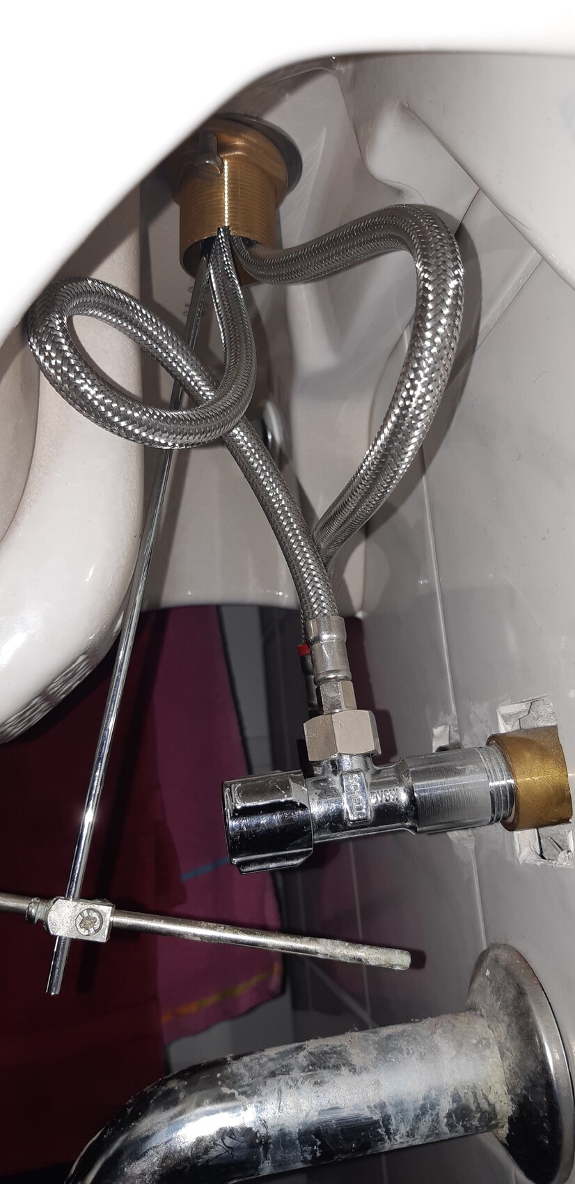 Unter dem Waschbecken sichtbare flexible Edelstahl-Schläuche, Ventil und Befestigungen.