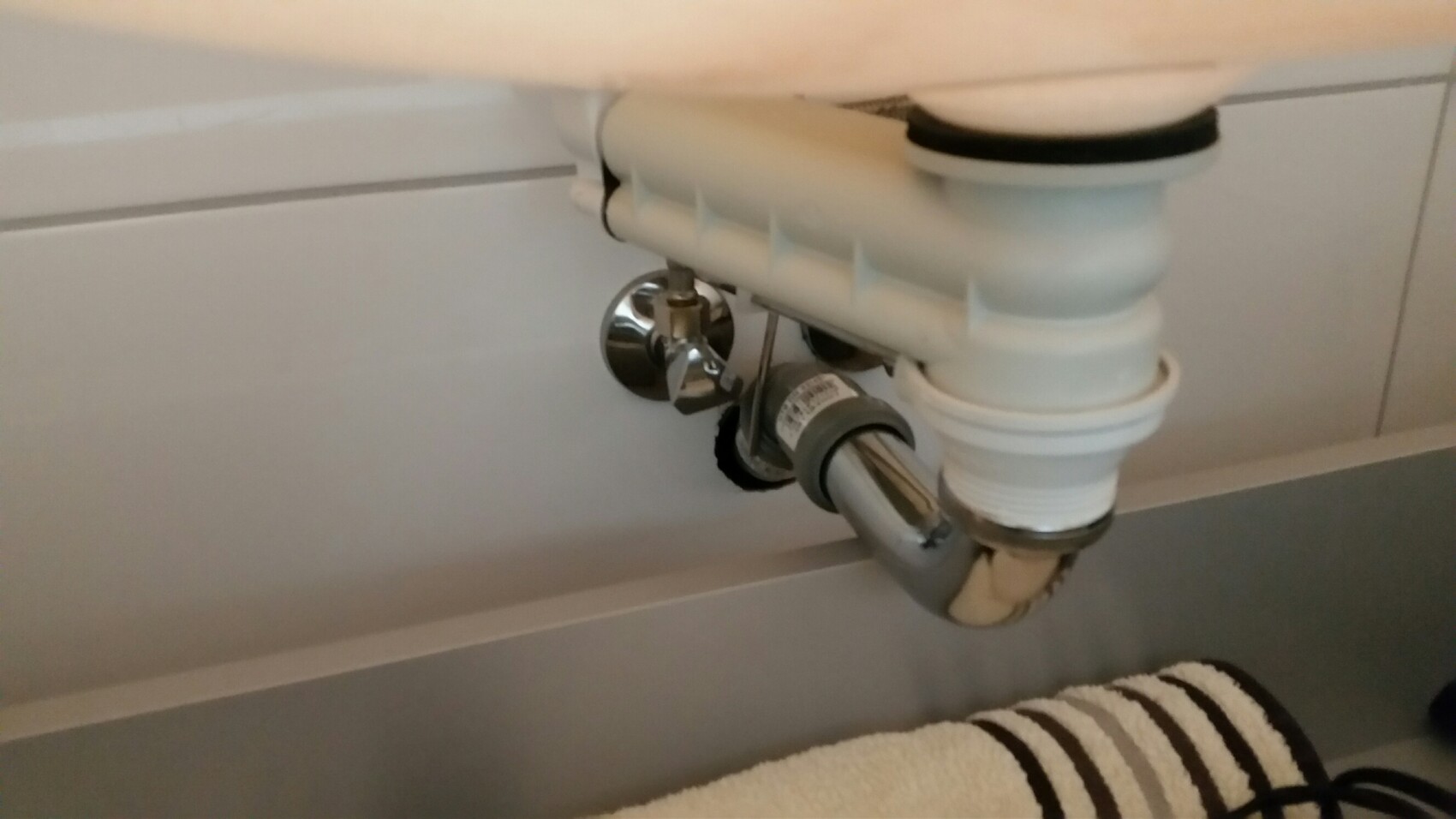 Unter dem Waschbecken sichtbares Siphon-Abflussrohr mit Absperrventil und Kunststoffteilen.