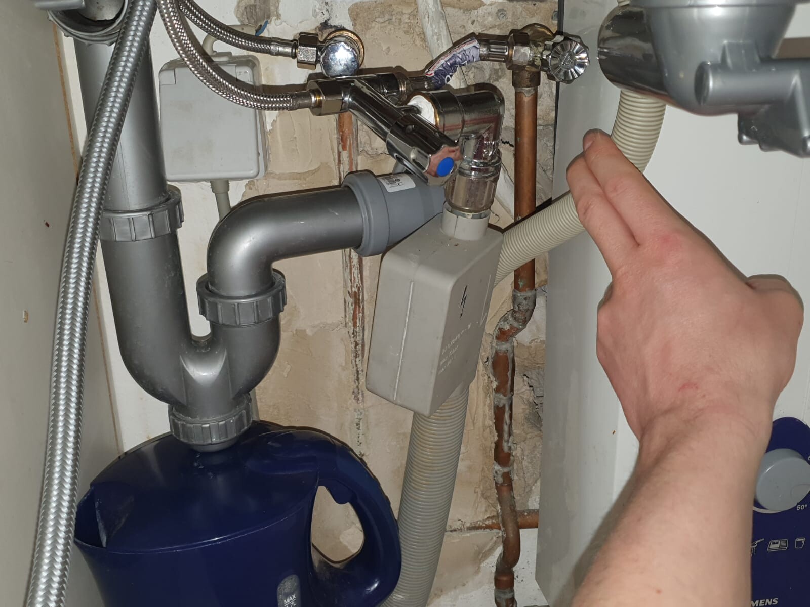 Unter dem Spülbecken: Siphon, Rohre, flexible Schläuche, Hand zeigt auf Absperrventil.