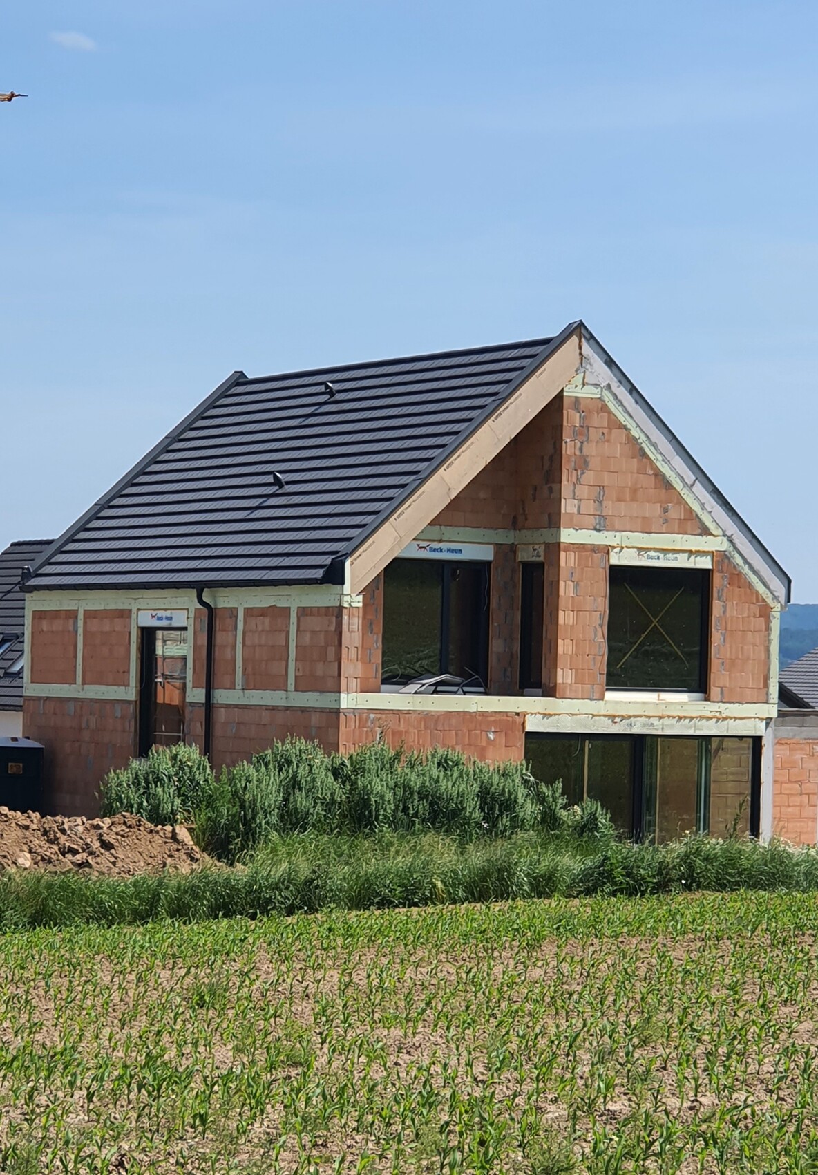 Unvollständiges Einfamilienhaus aus Backstein mit dunklem Ziegeldach im Bau, am Feldrand.