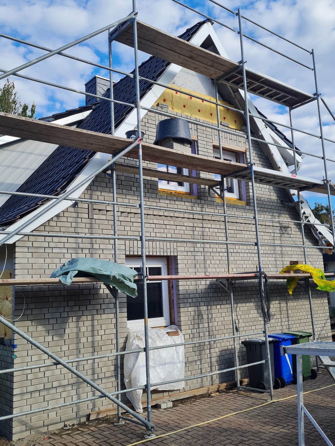 Einfamilienhaus unter Gerüst mit Dacharbeiten, Fensterrahmen und Bauzubehör vor der Fassade.