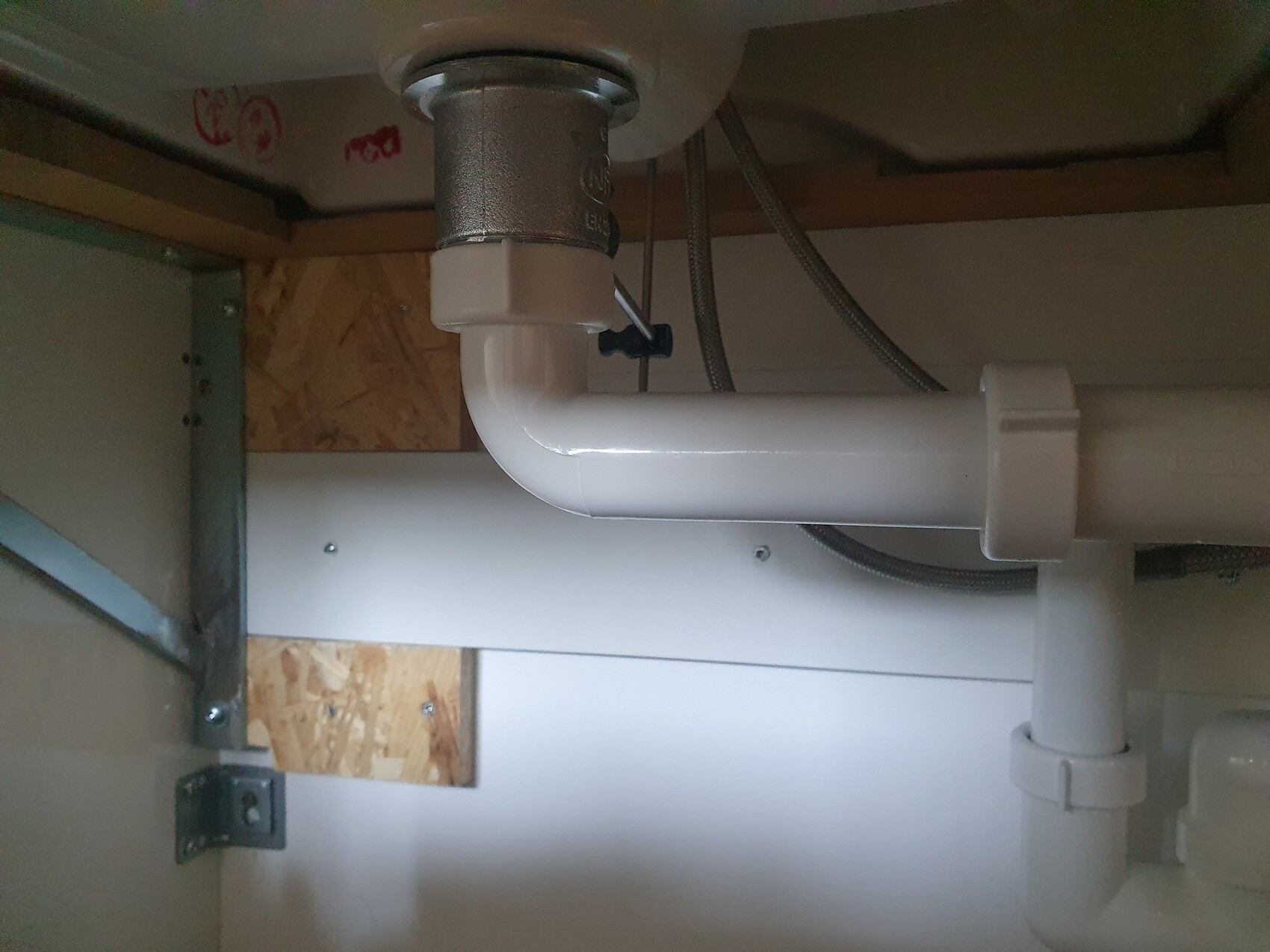 Unter dem Spülbecken: weißes PVC-Abflussrohr mit Bogen (P-Trap) und Metallfitting