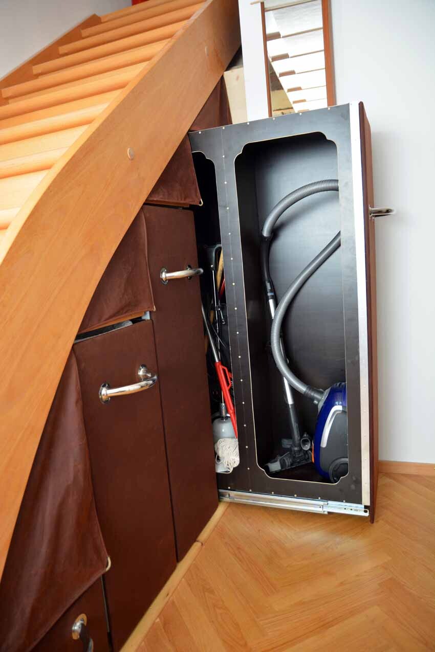 Unter dem Treppenaufgang geöffneter Schrank mit Staubsauger, Schlauch und Kabeln.