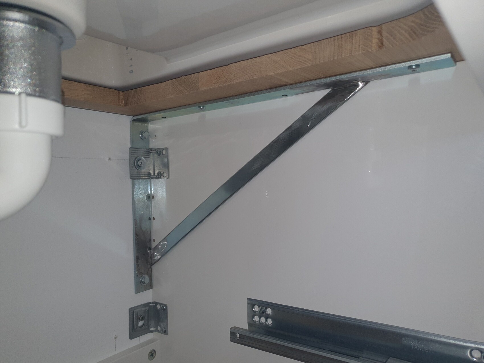 Unterseite eines Schranks mit Holzträger, diagonaler Metallstrebe und Auszugsschiene.
