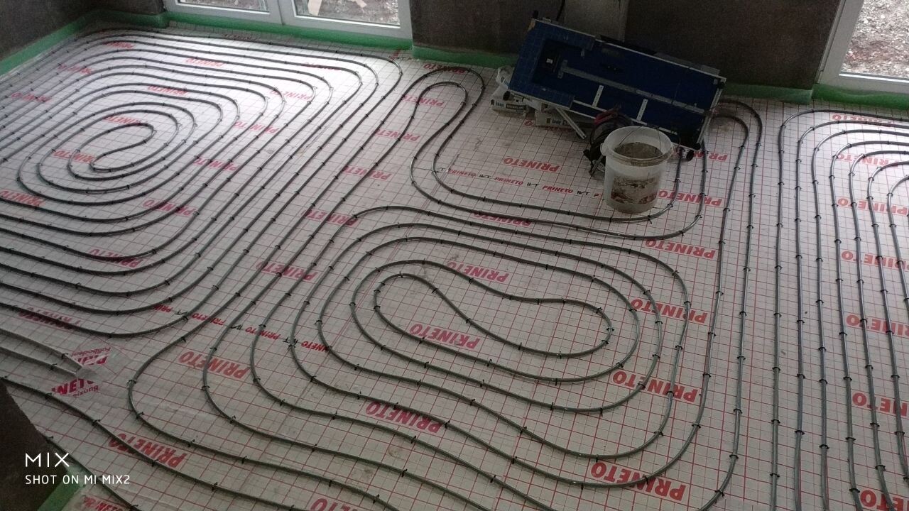 Unterflur-Heizungsrohre in Spiralen auf Dämmschicht, Baustelle mit Eimer.