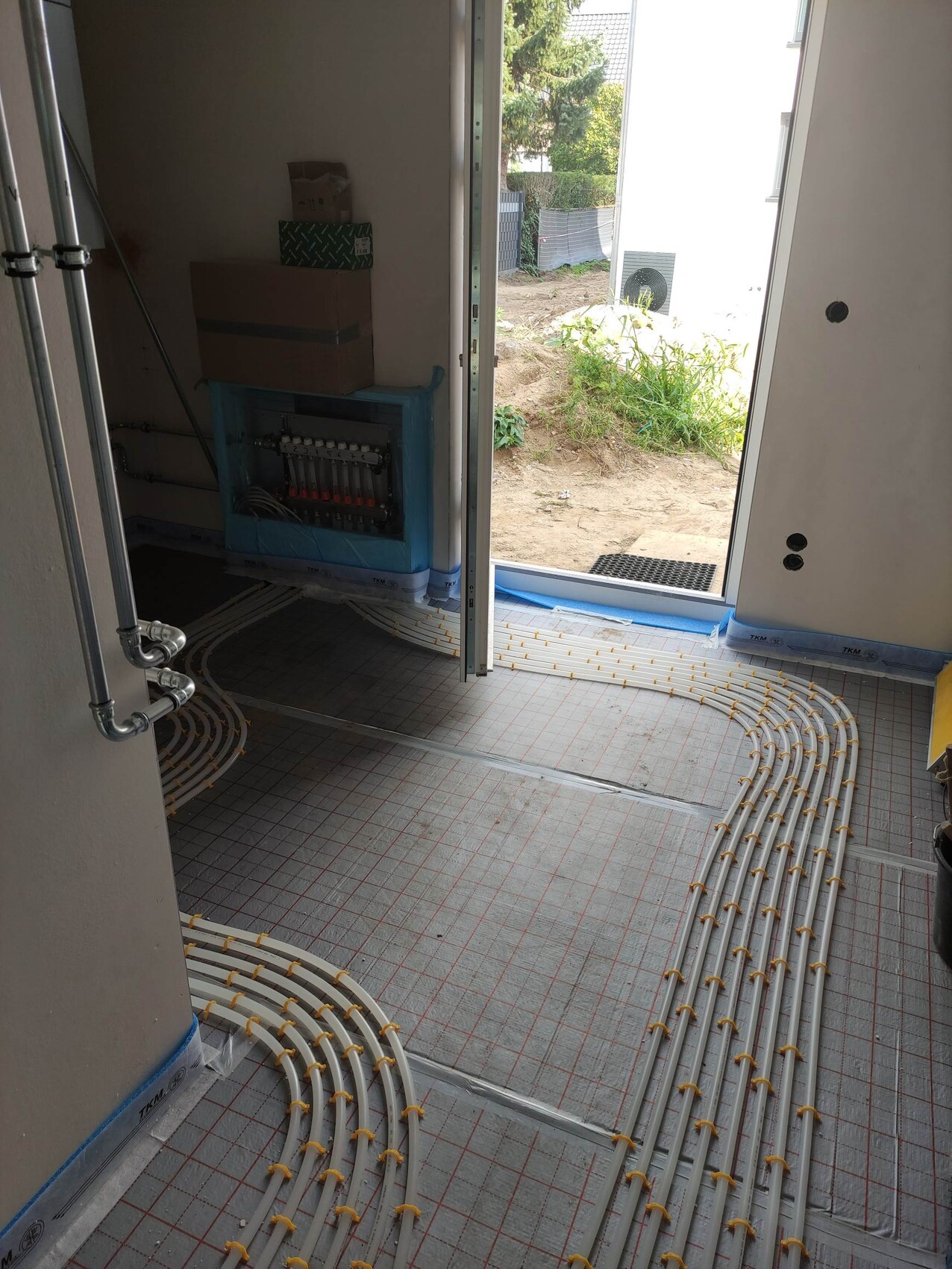 Innenraum einer Baustelle mit verlegten Fußbodenheizungsrohren, Tür nach außen offen.