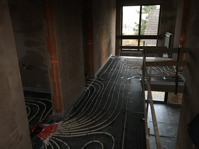Innenraum eines Bauprojekts mit verlegten Unterflur-Heizungsrohren, Holzgerüst und Fenster.