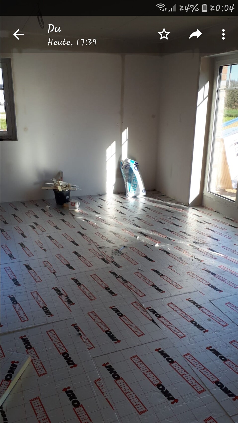 Unfertiges Zimmer mit Dämmplatten auf dem Boden und Bauutensilien am Fenster.