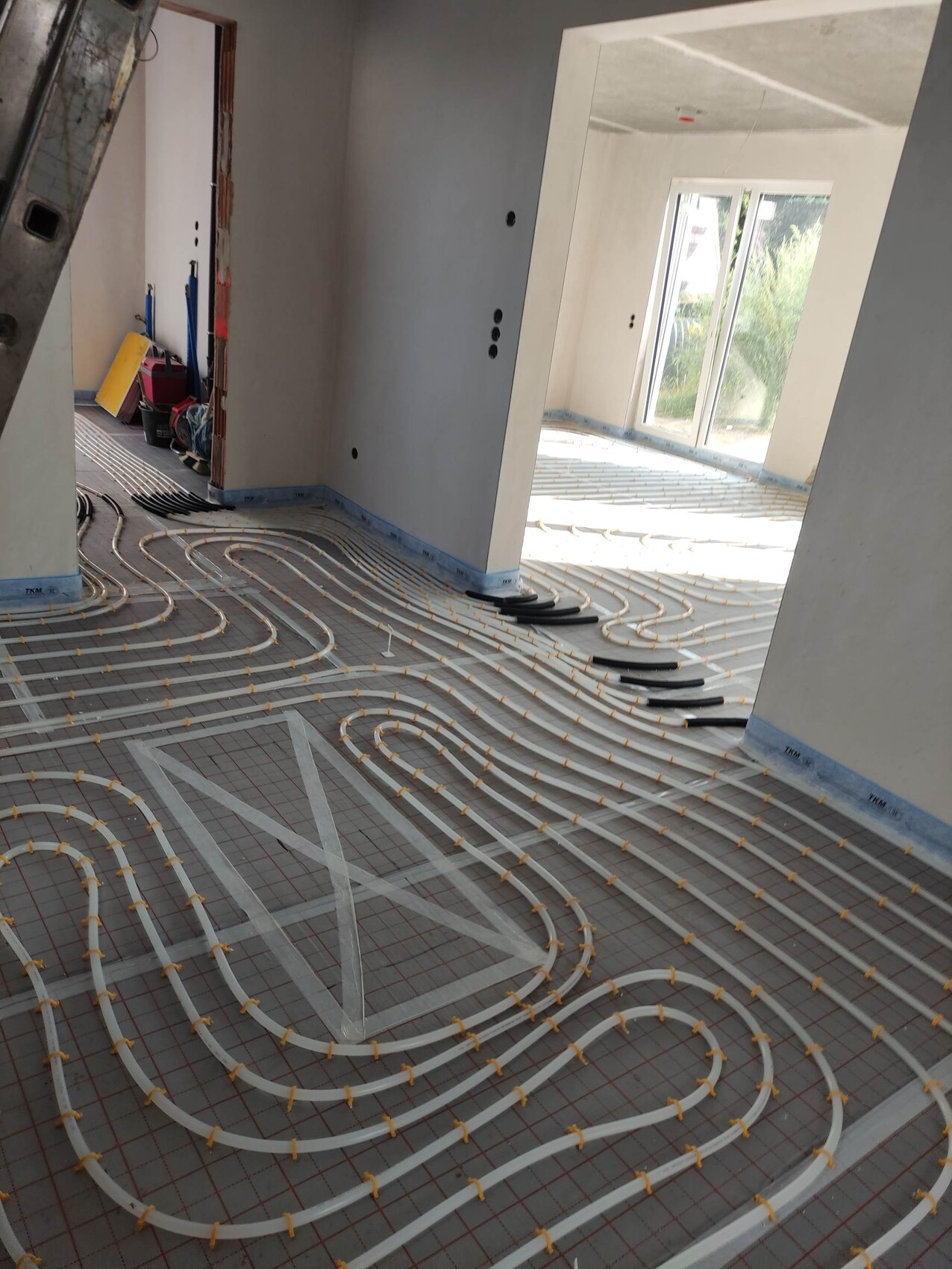 Unterbodenheizung: Weiße Rohre spiralförmig auf Rasterunterlage in unfertigem Innenraum verlegt.