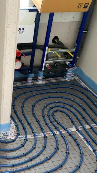 Unterflurheizung: Blau verlegte Schlauchkreise spiralförmig auf dem Boden neben Verteilerschrank.