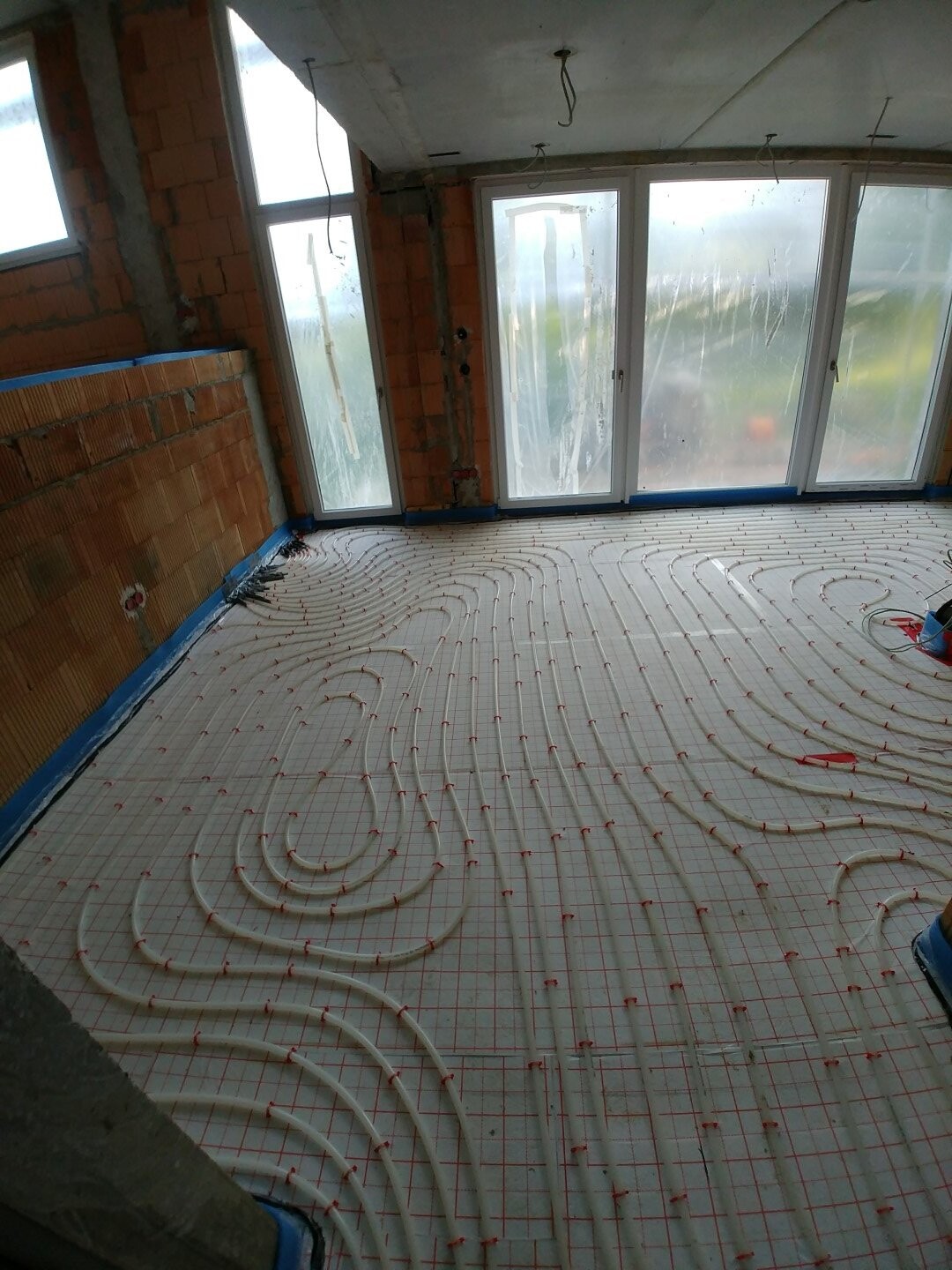 Bauzimmer mit verlegten Fußbodenheizungsschläuchen vor großen Glasfenstern