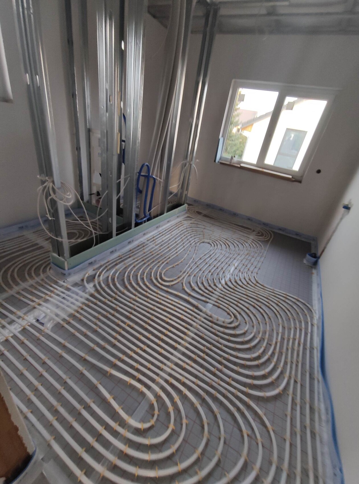 Unterbodenheizung: Rohrschlangen aus weißen Rohren im Baustellenraum, Metallständerwerk und Fenster.
