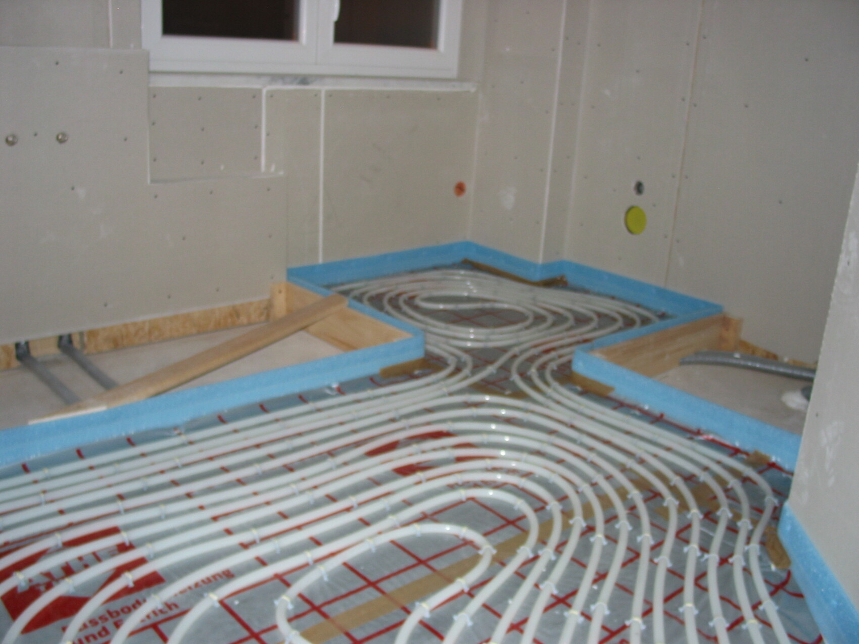 Fußbodenheizungsschläuche liegen spiralförmig auf Holzrahmen in einem Rohbau.