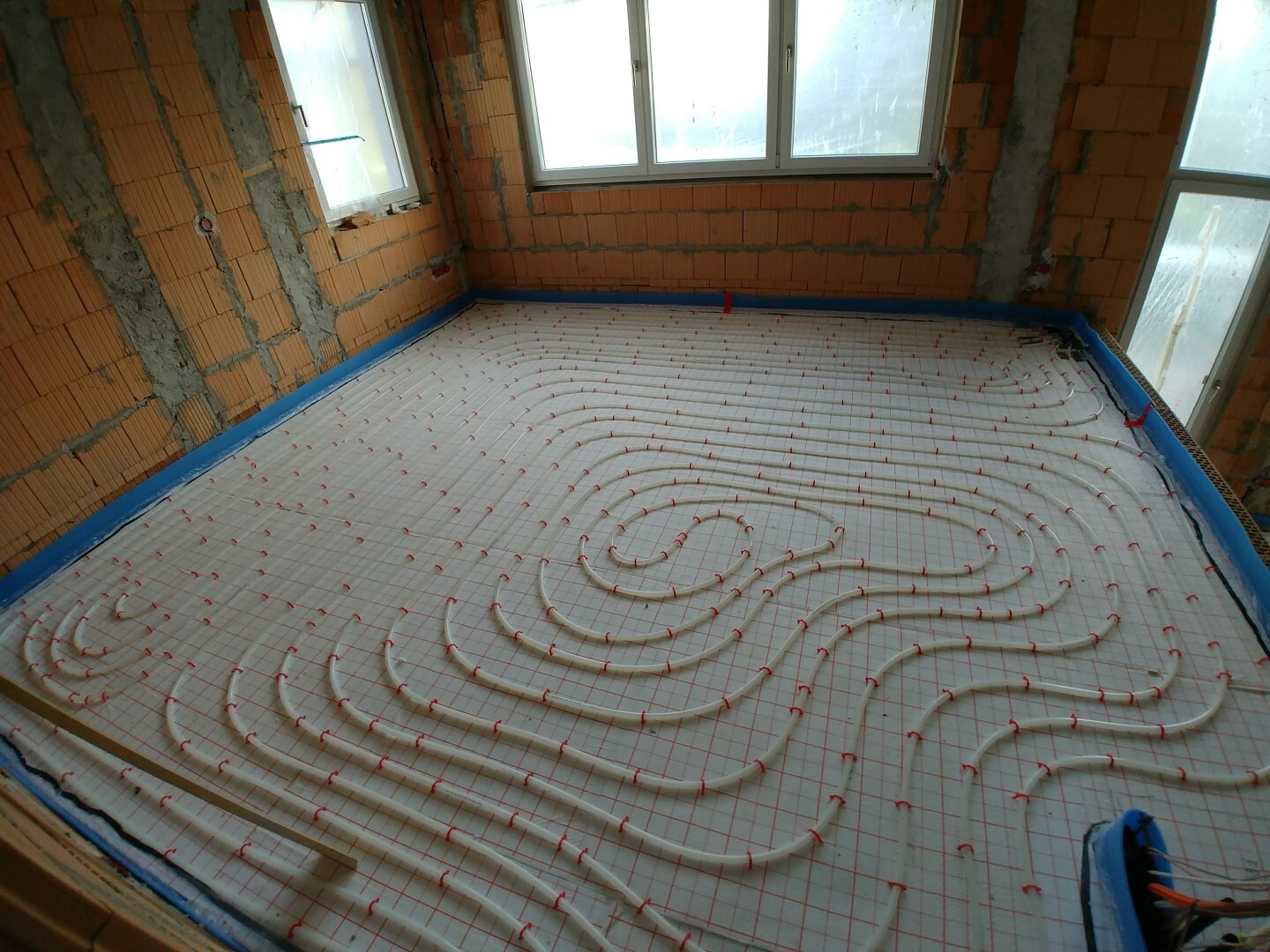 Rohbau mit Unterboden-Heizrohrsystem: Rohre in Spiralen auf Dämmplatte, Fensterfronten sichtbar.