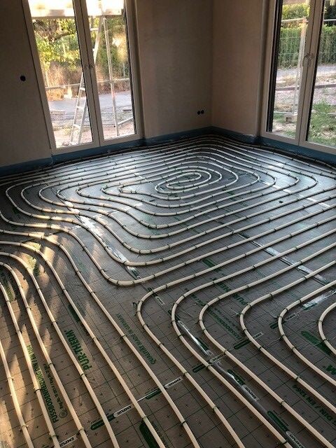 Unterboden-Heizrohre spiralförmig auf unfertigem Boden in einem Raum mit großen Fenstern