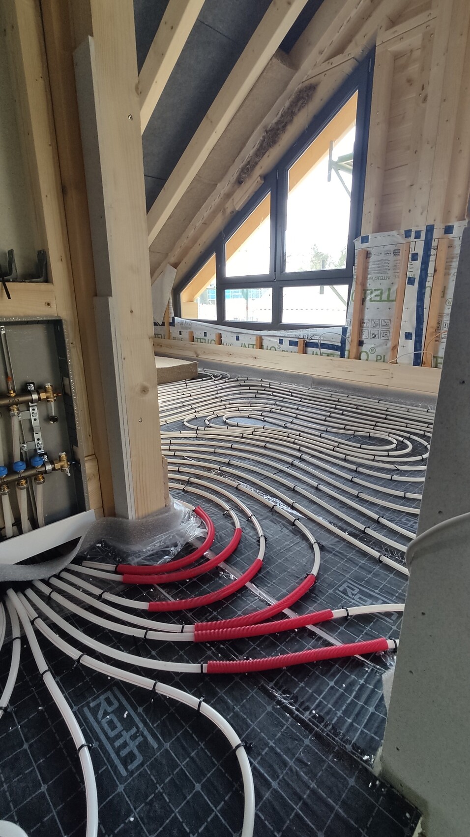 Verlegte Fußbodenheizungsrohre auf Dämmung in einem Holzständerwerk mit Dachfenstern.
