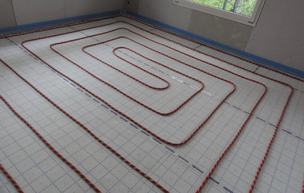 Unterbodenheizung: rotes Rohr spiralförmig in einer Bodenplatte verlegt, Baubereich.