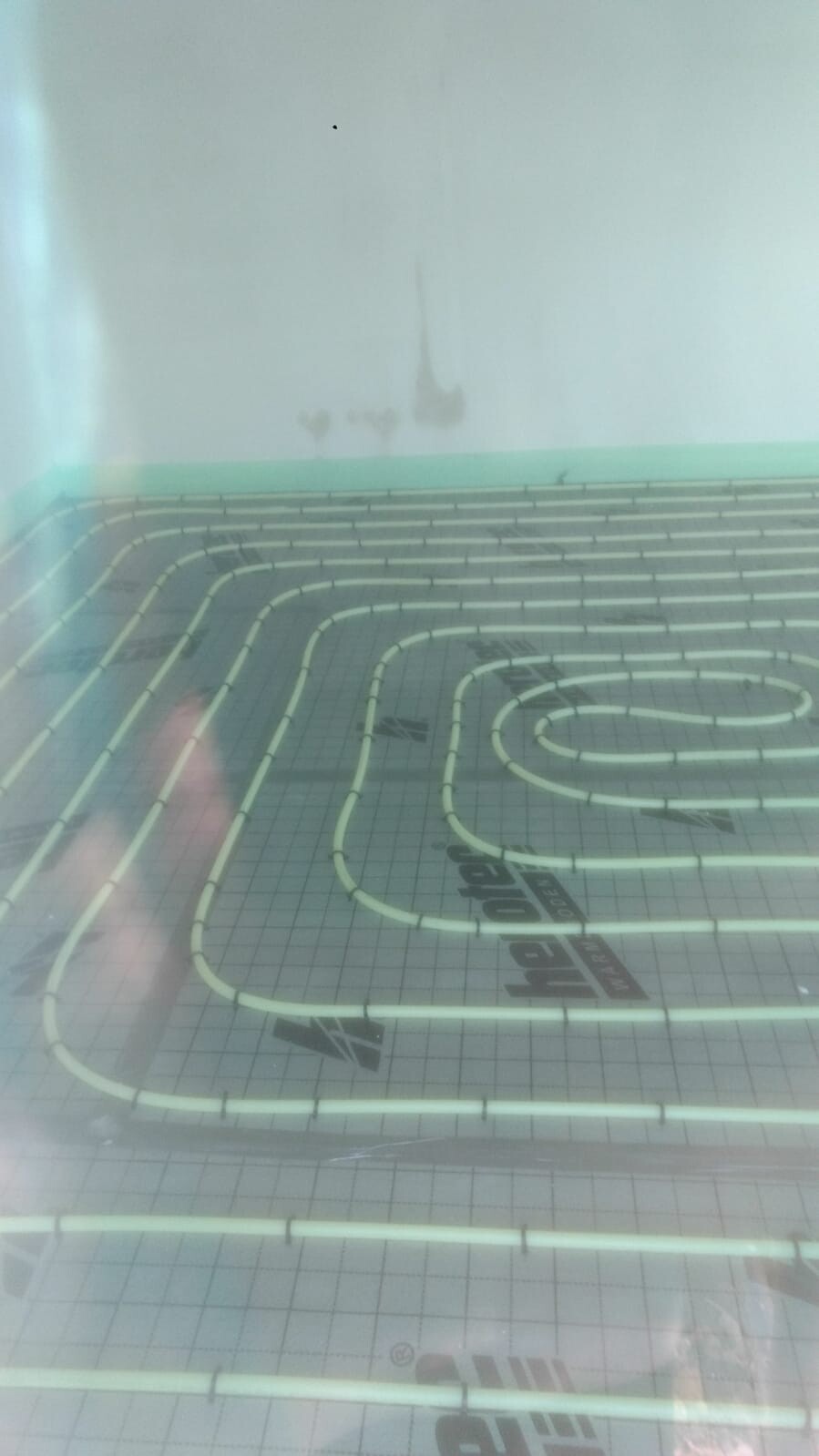 Fußbodenheizungsrohre spiralförmig auf Dämmunterlage in einem leeren Raum verlegt.