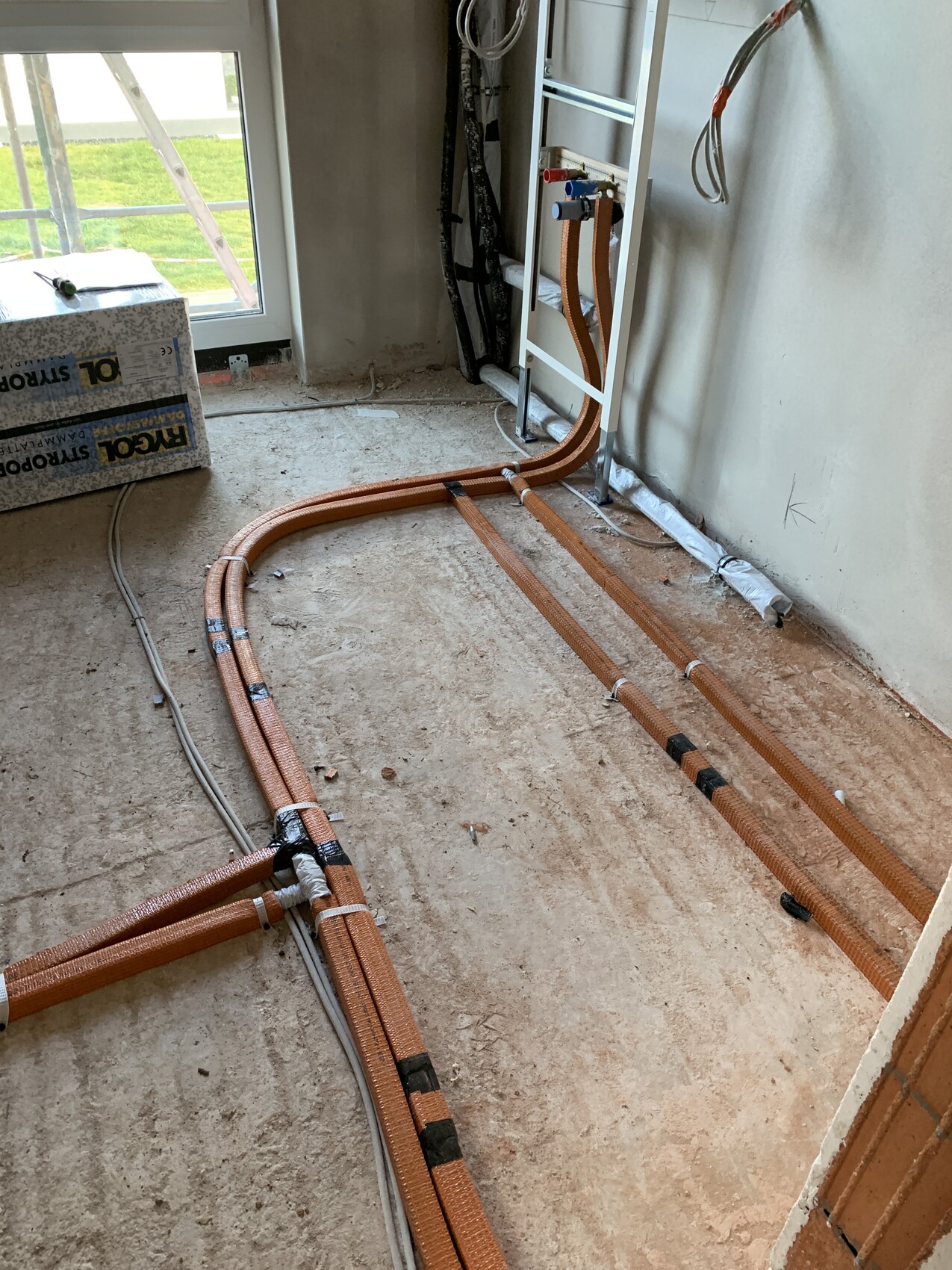 Innenraum-Baustelle: orange PEX-Heizungsrohre verlaufen im Boden, Kabel liegen daneben.