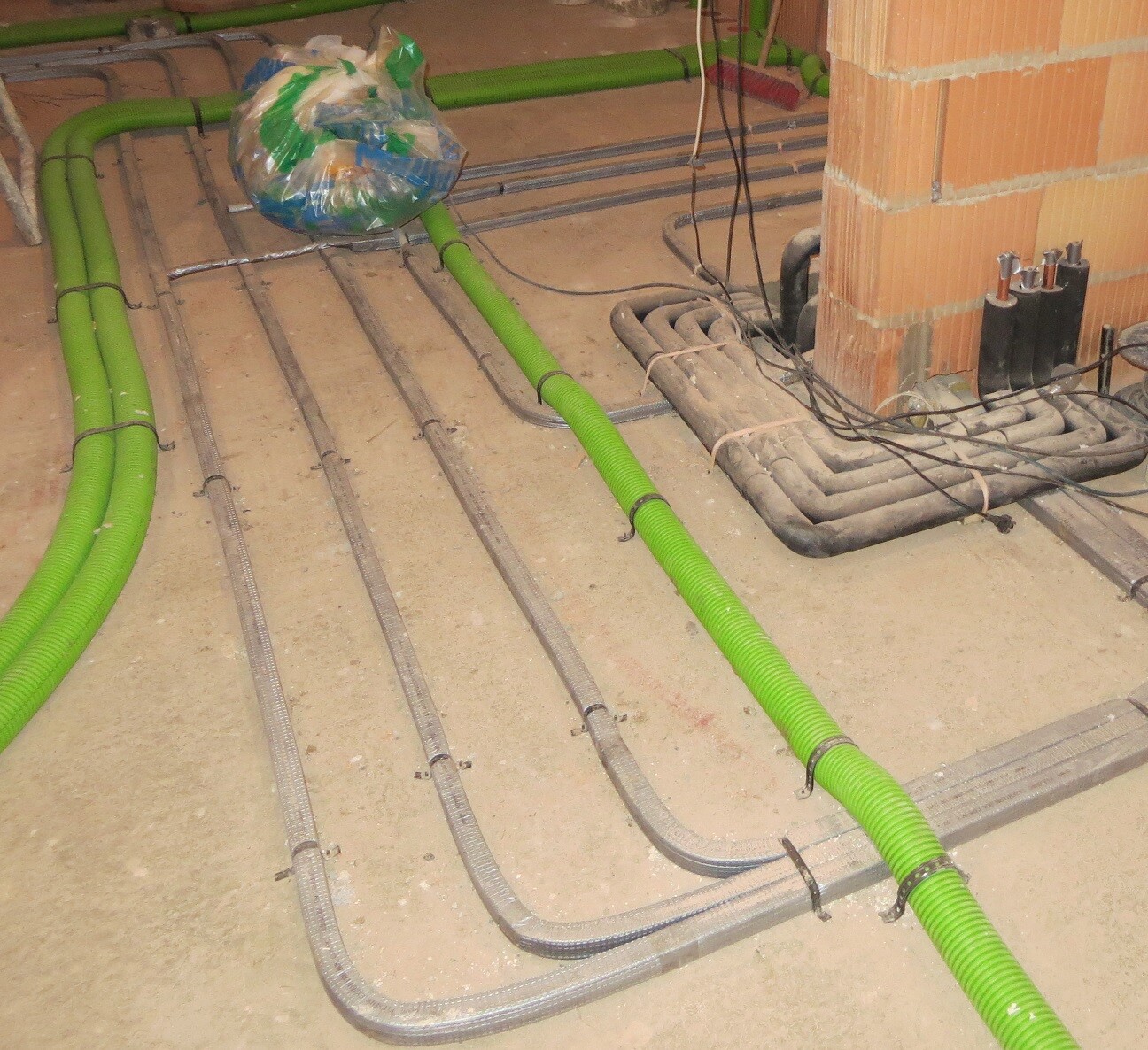 Grüne flexible Rohre und graue Metallrohre liegen auf dem Betonboden, Kabel liegen daneben.
