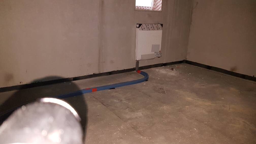 Baustellenraum im Untergeschoss mit Heizungsrohrinstallation und rohen Wänden.