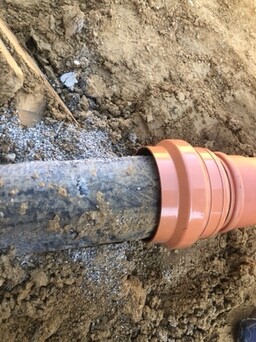 Unterirdische orangefarbene Abwasserleitung im Boden, Erdarbeiten sichtbar