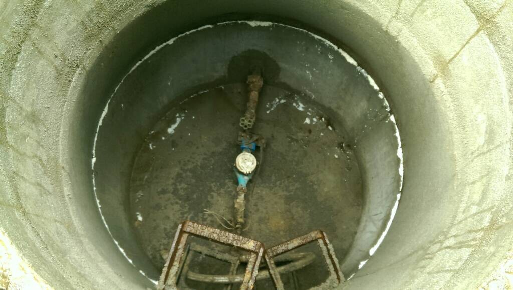 Runder Betongraben mit Wasserzähler, Rohren und rostiger Metallleiter