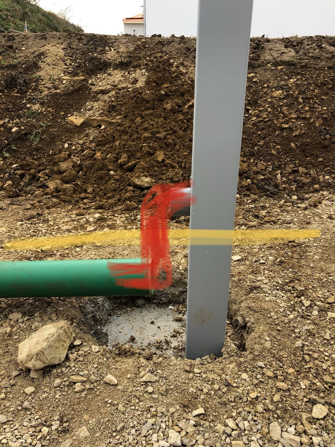 Baustelle mit grünem Rohr, grauer Stützsäule und Erdaushub