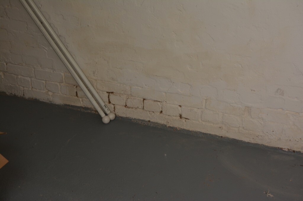 Kellerraum mit weiß gestrichener Ziegelwand, Rohboden und Installationsrohr