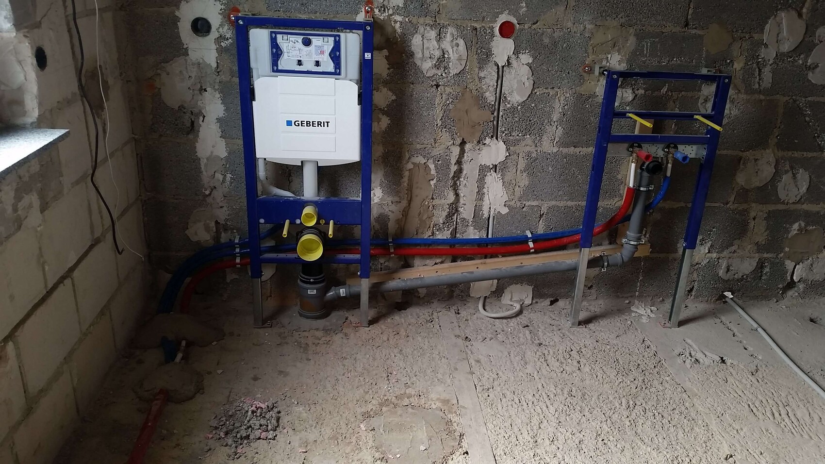 Geberit Installationsrahmen mit Spülkasten; blaue und rote Sanitärrohre im Rohbau.