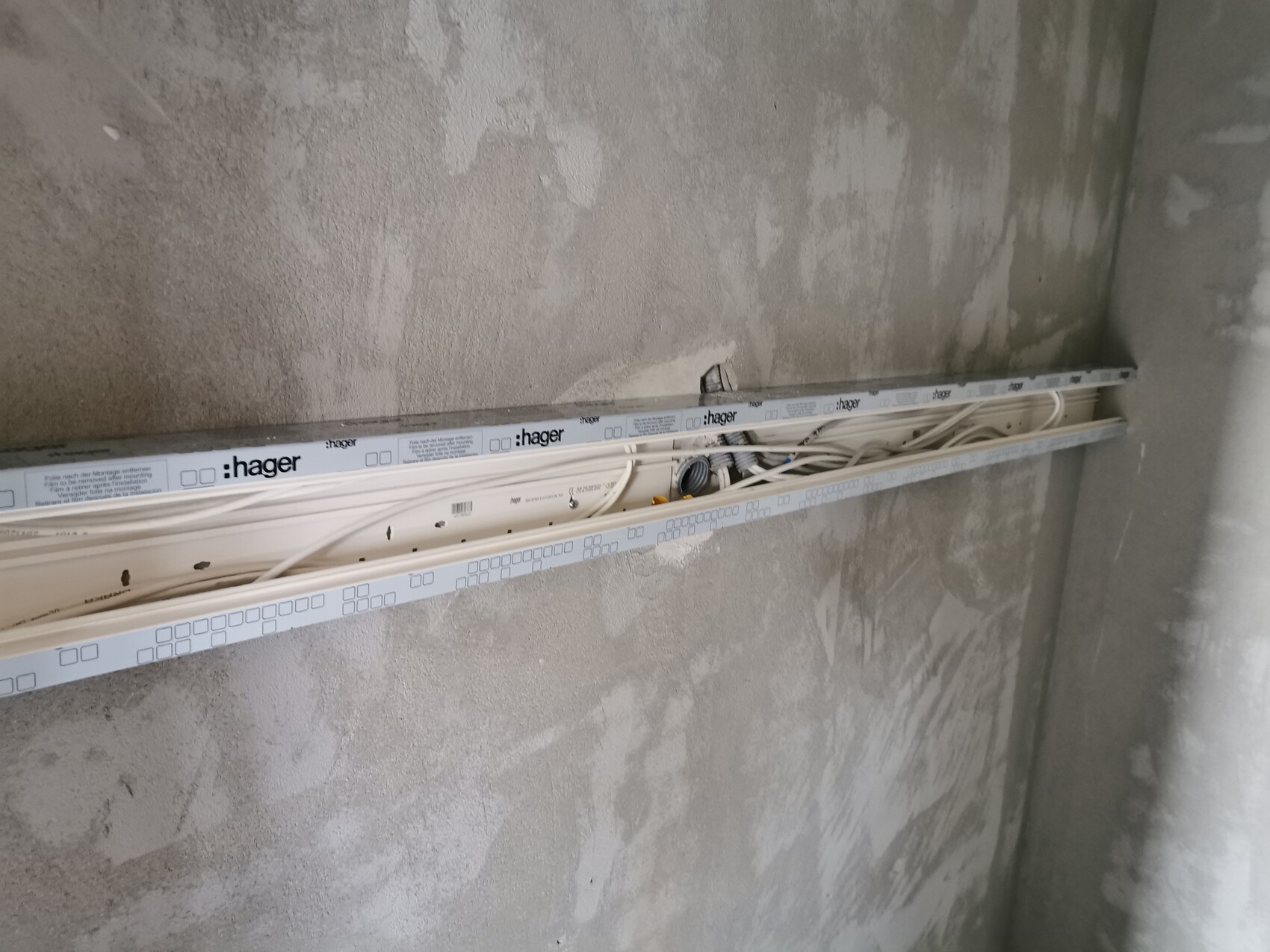 Kabelkanal mit mehreren Kabeln an einer rohen Betonwand, Hager-Tragschiene sichtbar.