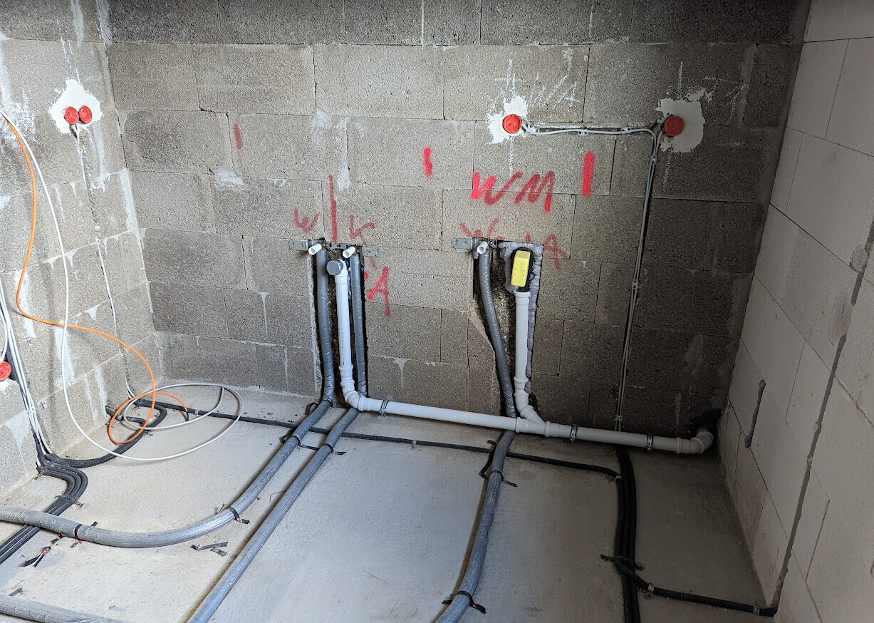 Baustellenzimmer mit sichtbaren Wasserleitungen, Elektrorohren und roten Markierungen an der Wand.